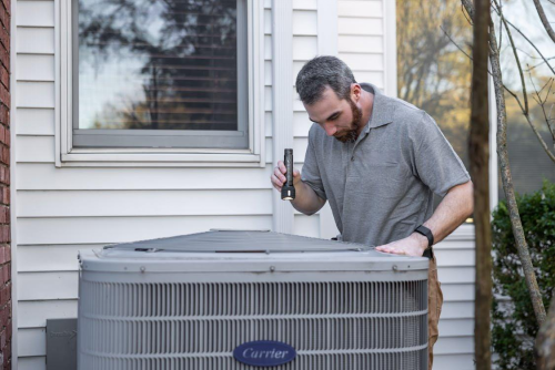 An HVAC technician inspecting an outdoor air conditioning unit with a flashlight